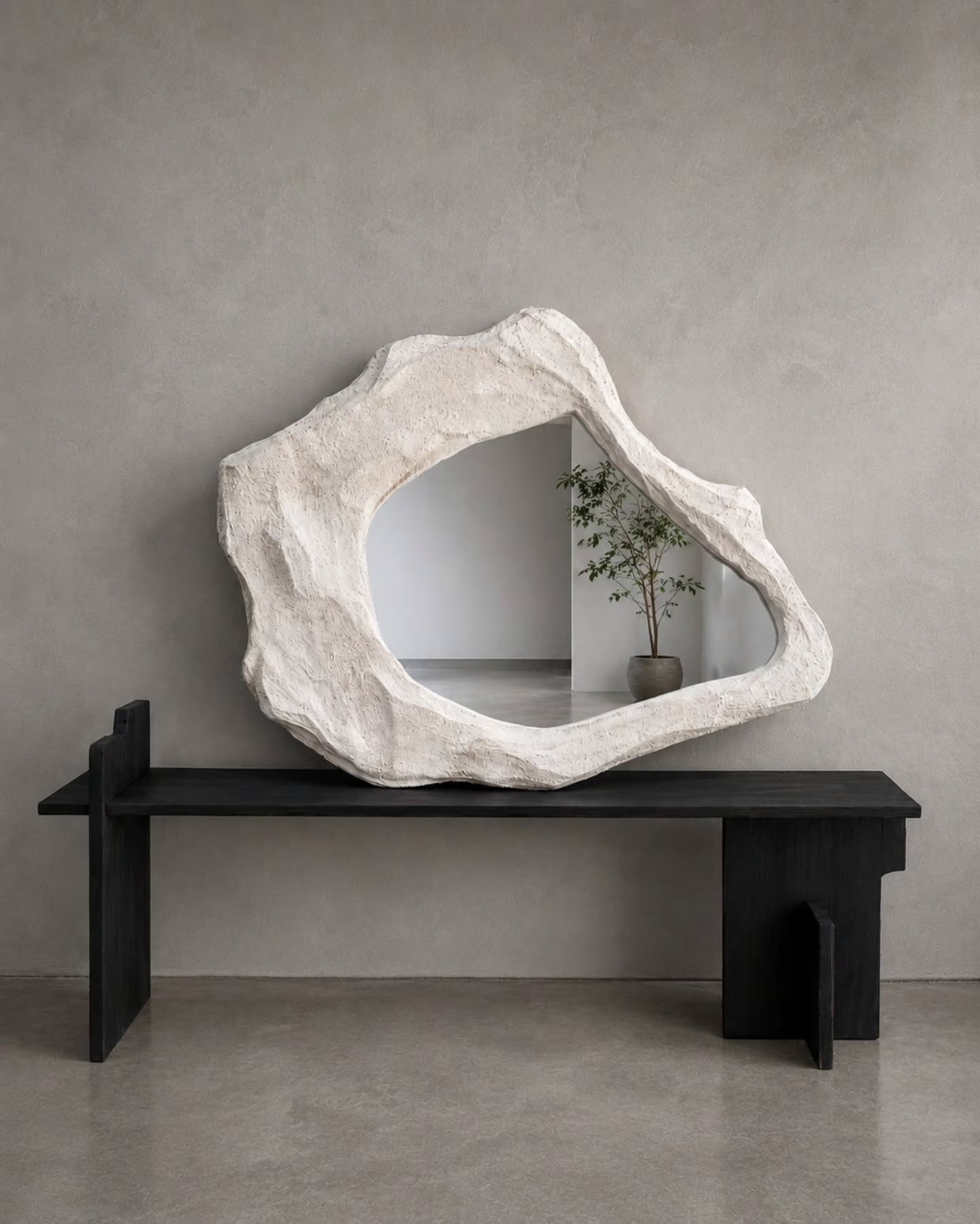 Origen, BN 005: espejo de contorno orgánico y superficie mineral ocupando el muro del espacio que lo recibe.